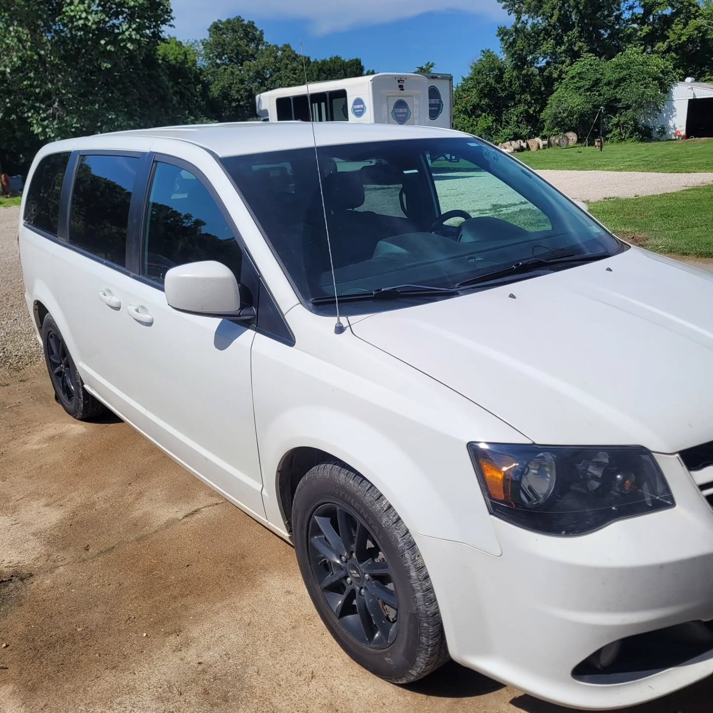 White Dodge Grand Caravan parked on a driveway under summer trees