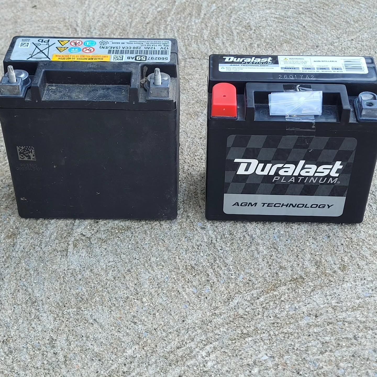 Old auxiliary battery beside a new Duralast replacement on concrete