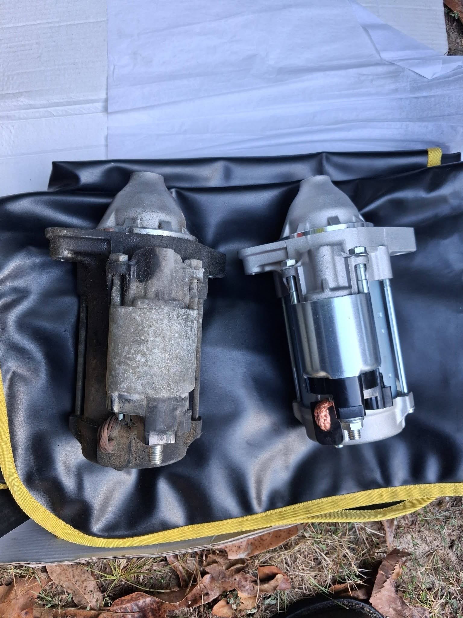 Worn starter motor beside its new replacement on a fender cover